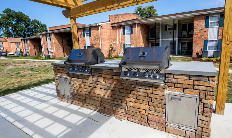 Two grills on a cement pad in front of an apartment complex